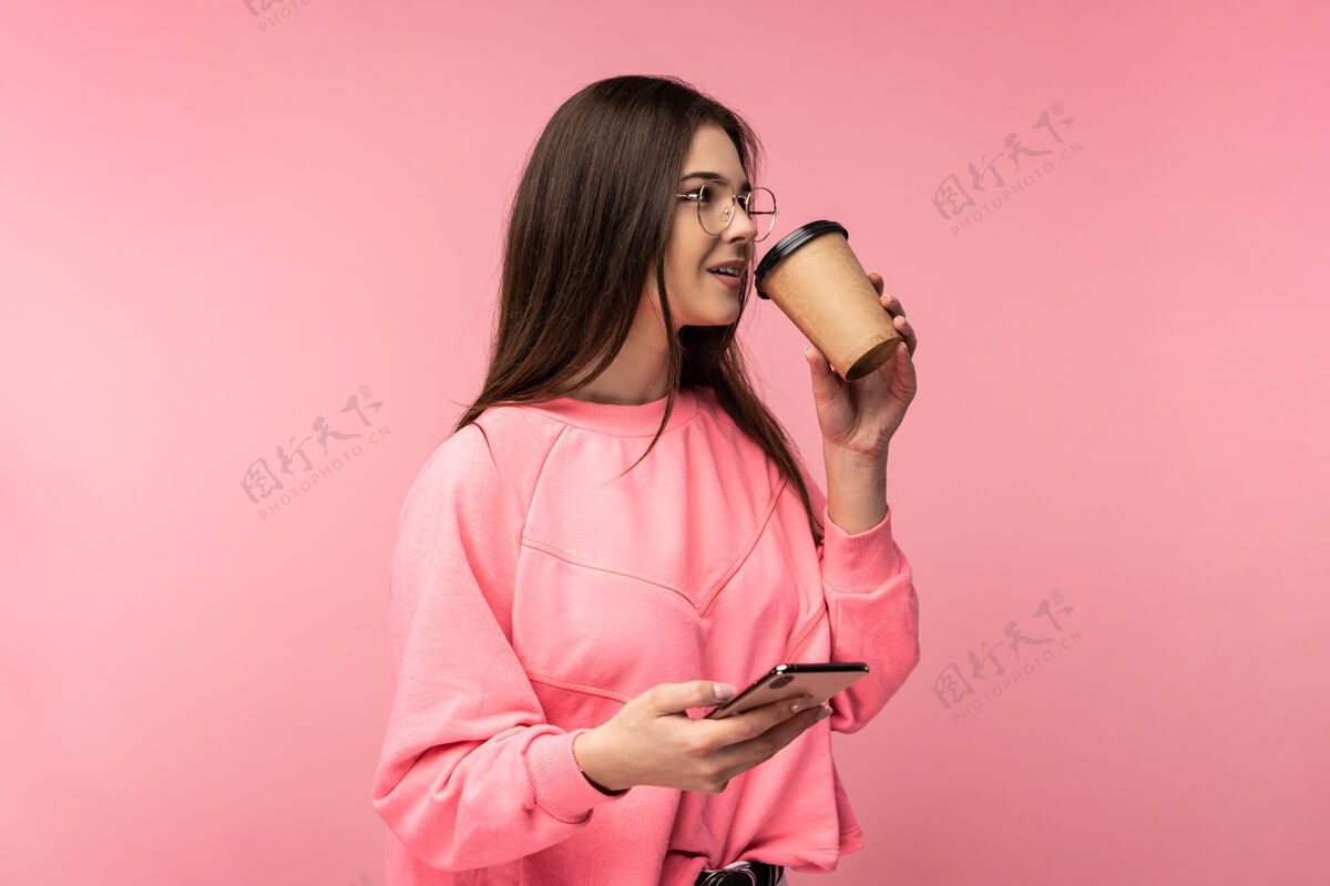 享受戴着眼镜的美女喝着咖啡茶 拿着智能手机的照片快乐情绪幸运
