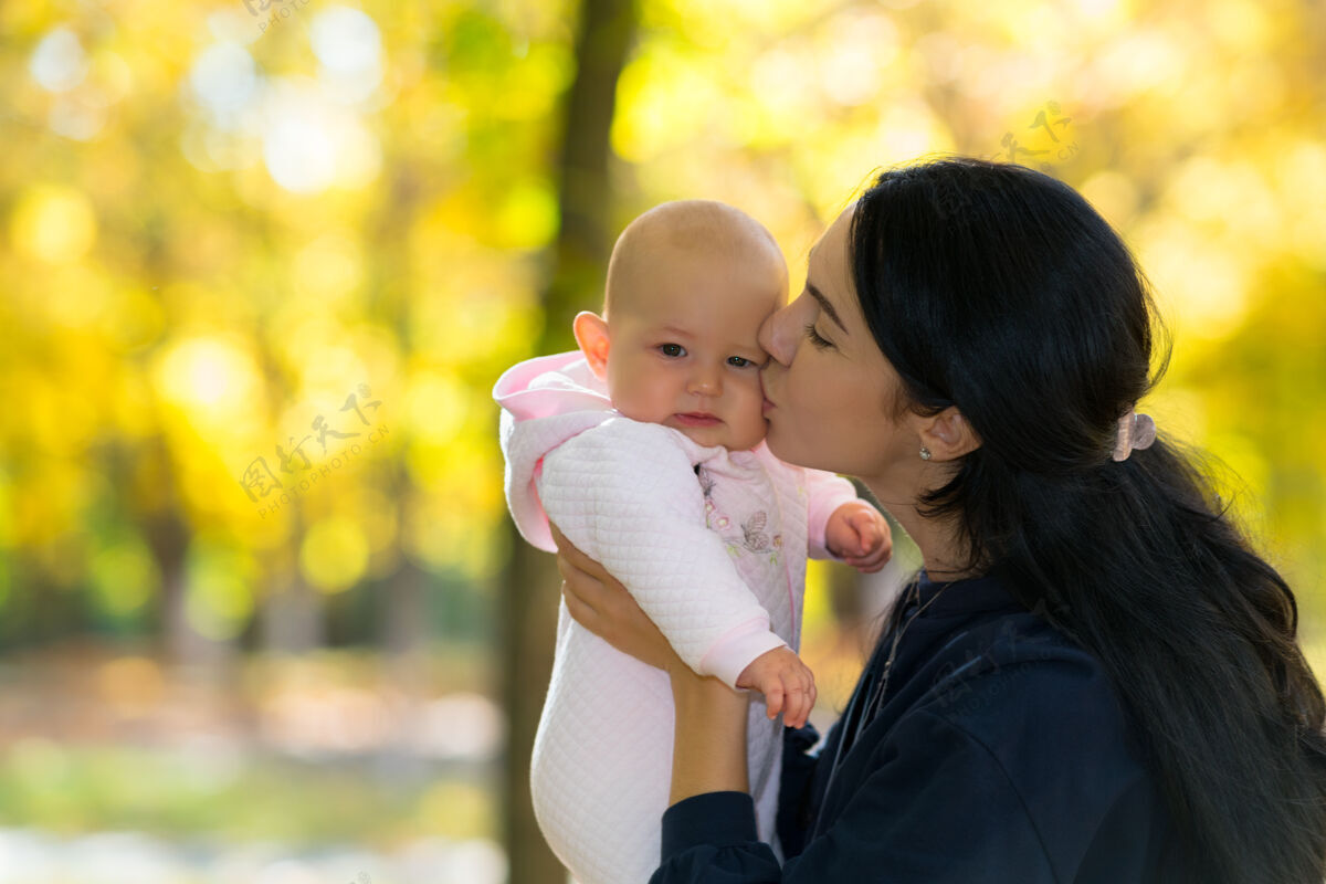 肩膀在一个明媚的秋天公园里 一位母亲深情地亲吻着她的孩子的脸颊树叶情感父母