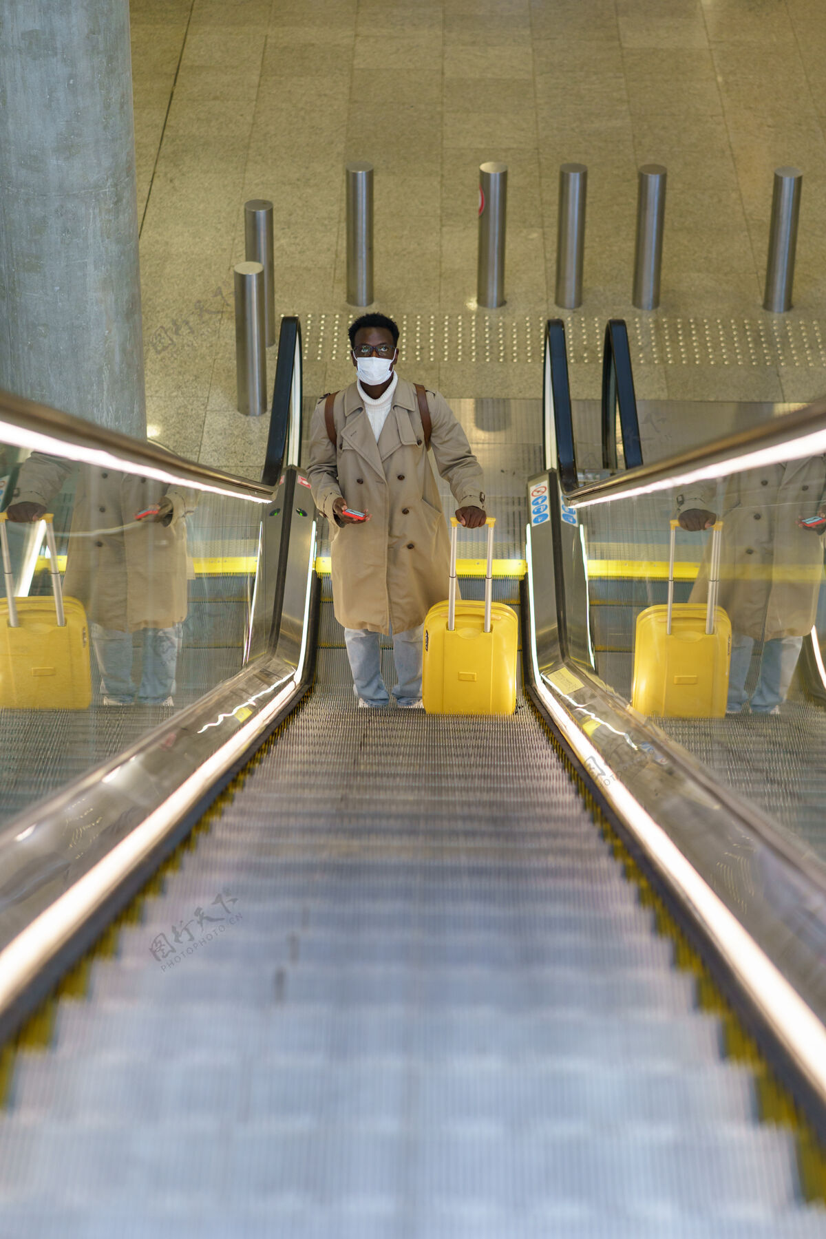 病毒携带手提箱的黑人男子站在机场的自动扶梯上 在covid-19流感大流行期间戴口罩交通工具旅行者行李