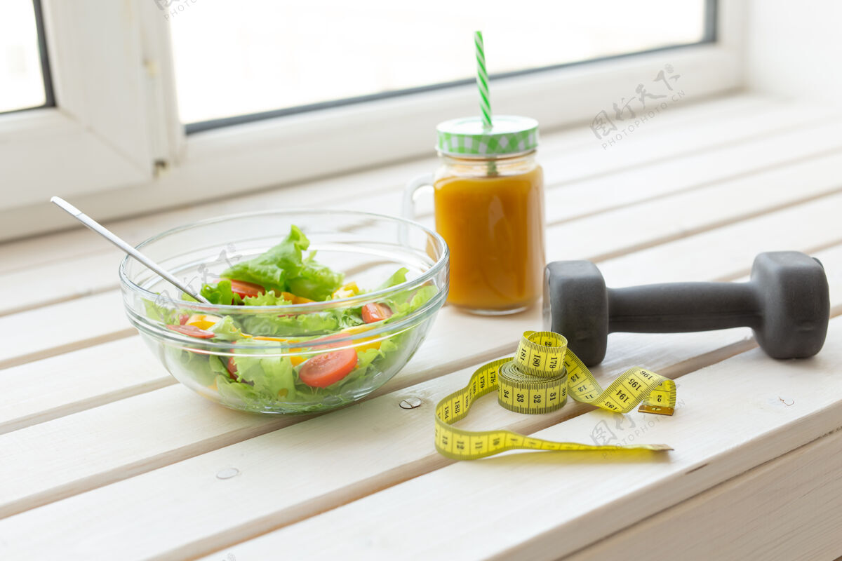 无人蔬菜沙拉 水果冰沙和哑铃躺在白色的床上窗台.concept健康的生活方式 体育锻炼和适当的营养窗台玻璃自然