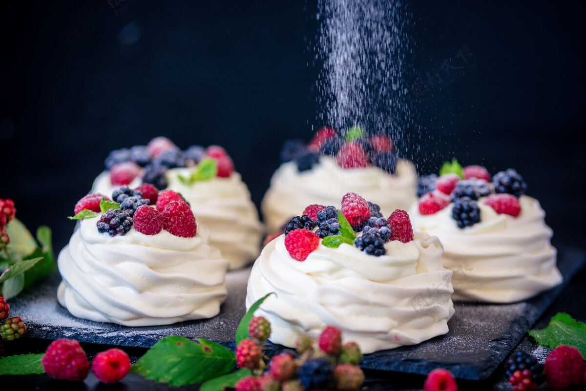 蛋白酥皮巴甫洛娃蛋糕的自制蛋白酥皮 配以新鲜蓝莓 黑莓和糖粉 表面为黑色混凝土纹理美味美味美味