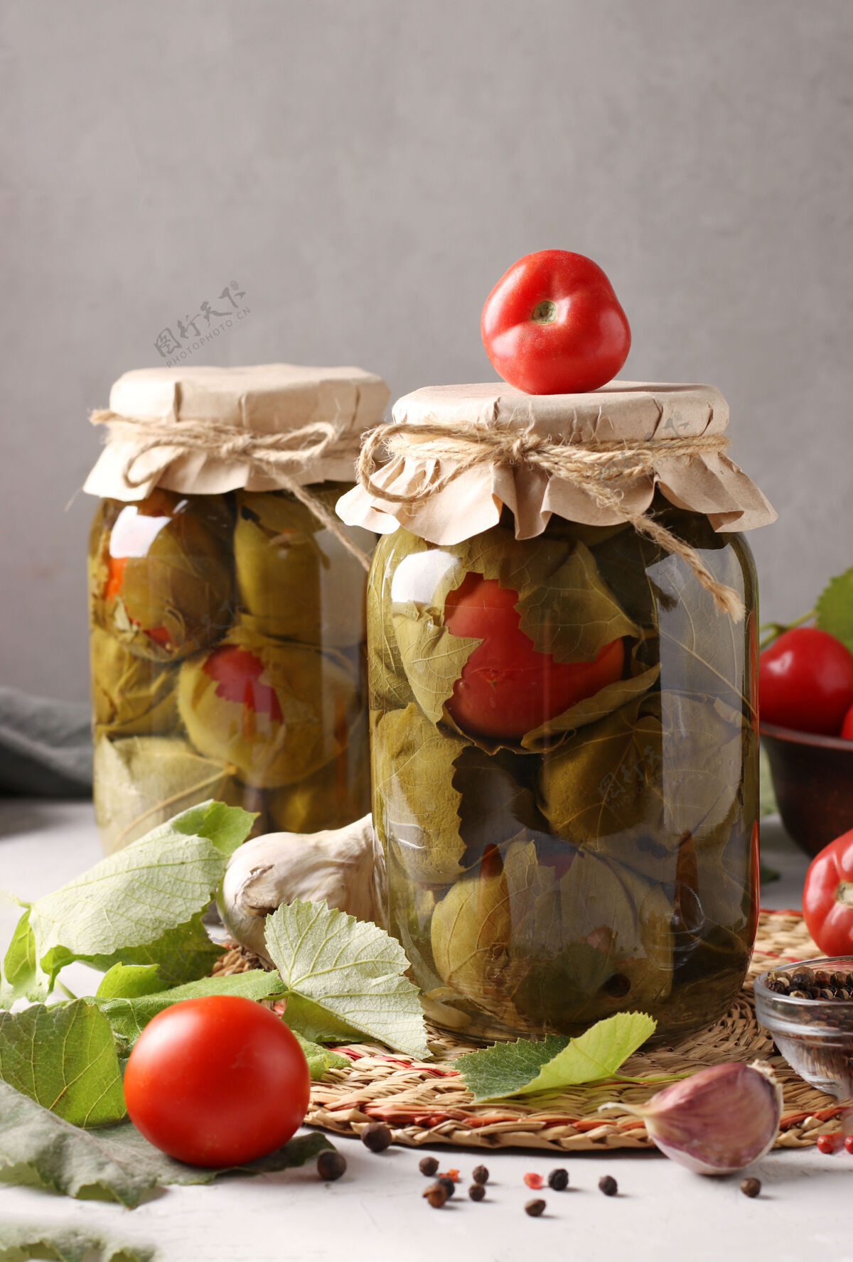 生产在灰色表面的两个玻璃罐中用葡萄叶腌制西红柿和大蒜烹饪银行水