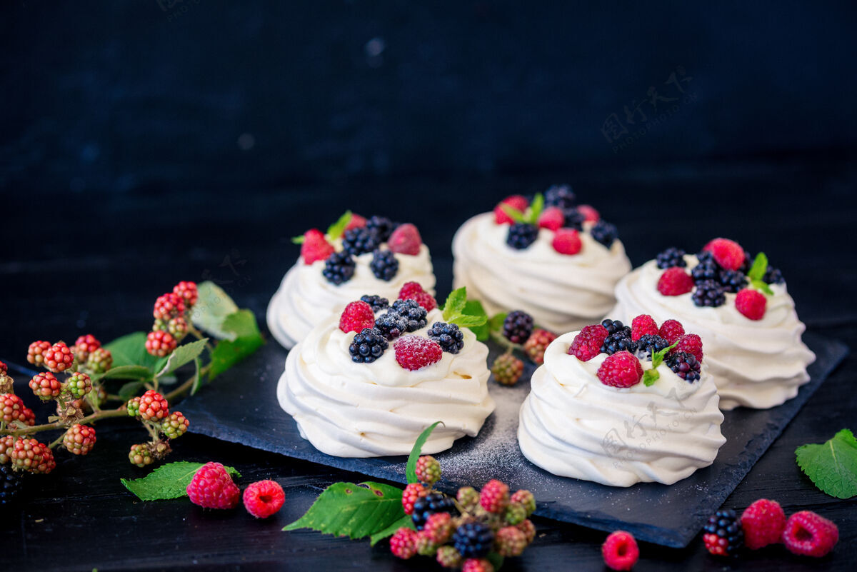 食物巴甫洛娃蛋糕的自制蛋白酥皮 配以新鲜蓝莓 黑莓和糖粉 表面为黑色混凝土纹理蓝莓黑莓年份
