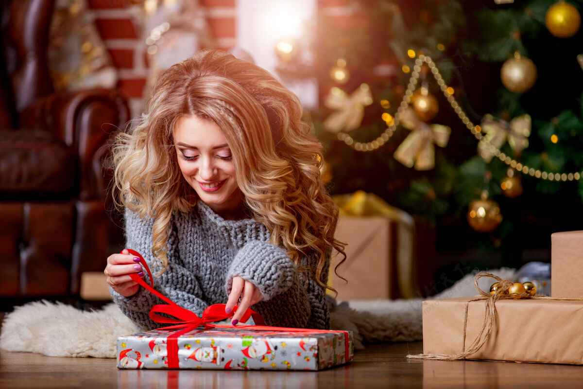 女人圣诞树旁穿毛衣的女孩正在打开礼物快乐女人圣诞