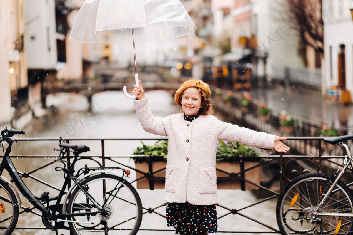 城市一个穿着外套 带着透明雨伞的开朗漂亮的女孩法国女孩在雨中高高兴兴地撑伞天空城市伞