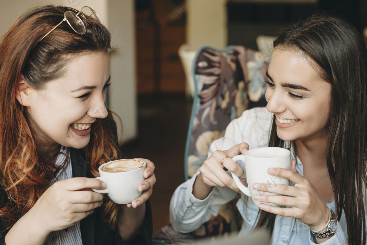 微笑两个美女一边喝咖啡一边笑一边讲故事一边坐在咖啡馆里互联网屏幕吃