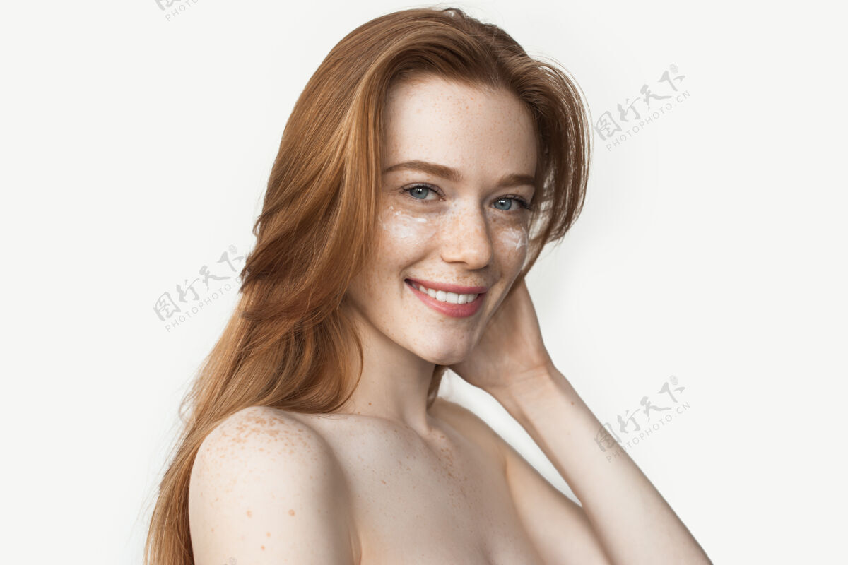 完美无瑕满脸雀斑的白种女人 姜黄色头发对着镜头微笑 赤裸的肩膀和眼霜摆姿势牙齿微笑美容特写