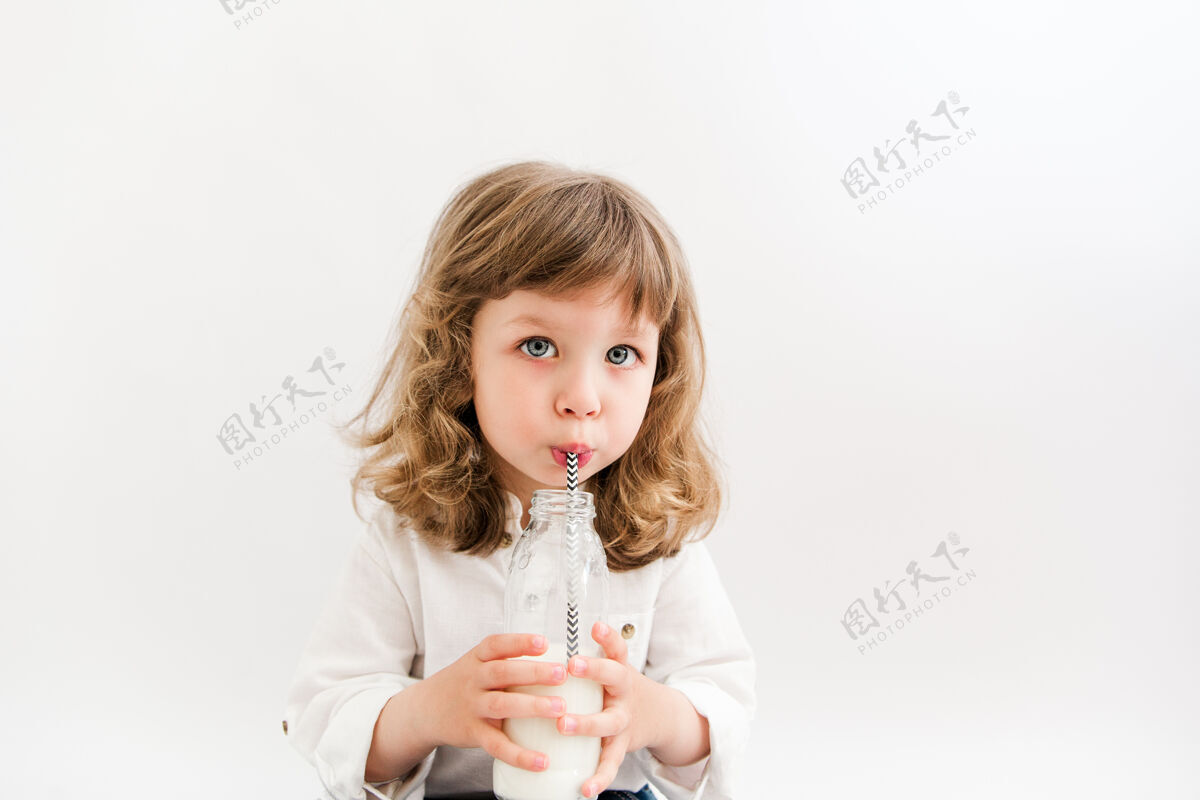 饮食卷发蓝眼睛的漂亮女孩喝着瓶子里的牛奶营养饮用室内