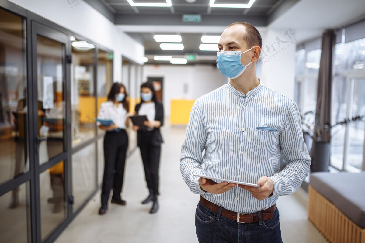 人优雅的商人戴着医用口罩站在办公室走廊里 手里拿着一块药片纸张护理流行病