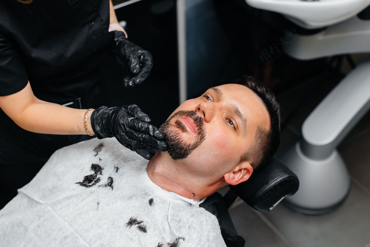 锋利一个专业的发型师在一个现代时尚的理发店剃须和削减一个年轻人的头发护理剪刀修剪