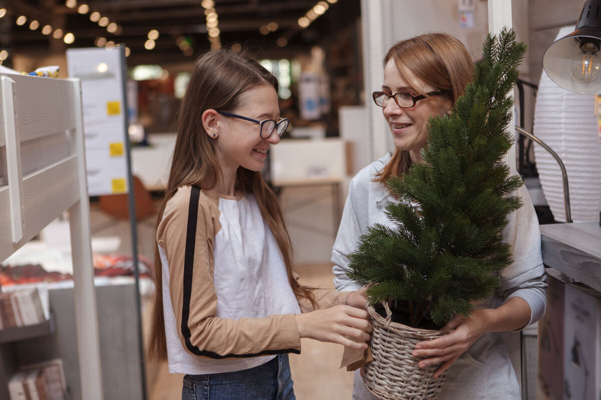 庆典十几岁的女孩和她的母亲在家具店买圣诞树壶节日传统