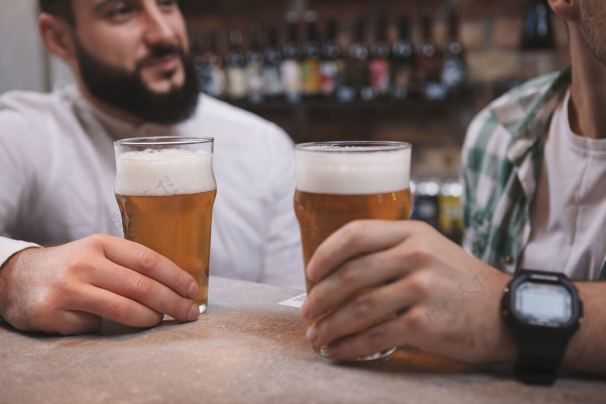 朋友男性朋友在酒吧聊天时拿着啤酒杯的不规则特写镜头谈话酒吧饮酒