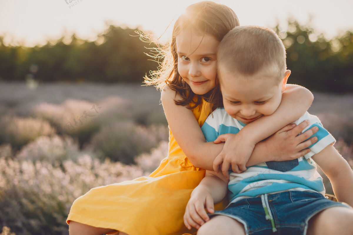 日落可爱的小女孩在夕阳下和花丛中拥抱着她的弟弟温柔表情田野