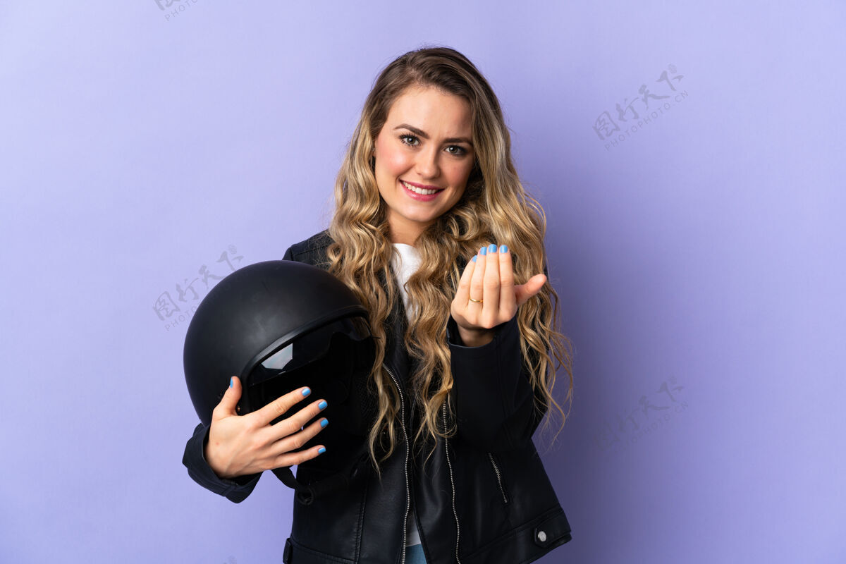 摩托车手巴西一名年轻女子手持一顶摩托车头盔 被隔离在紫色背景上 邀请前来手高兴你来了驾驶演示年轻人