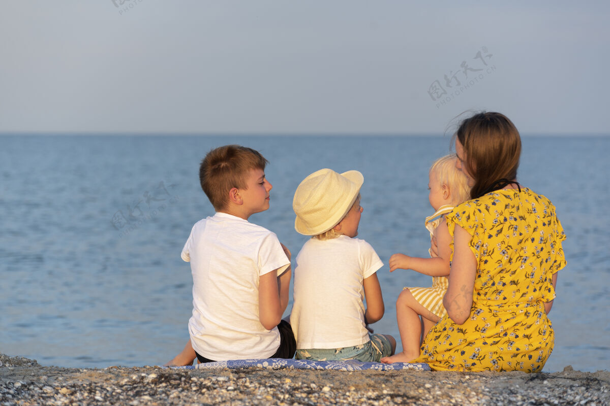 爱带着三个孩子的年轻母亲正在床上休息海边后面视图.族在海边度假小两个妈妈