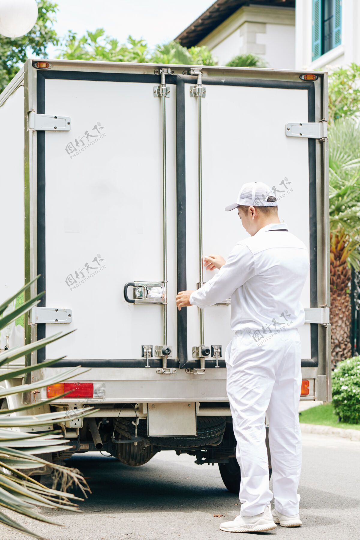 卸货一个身穿白色制服的送货员在把牛奶瓶装上货车后 关上了货车后备箱的门服务工作箱子