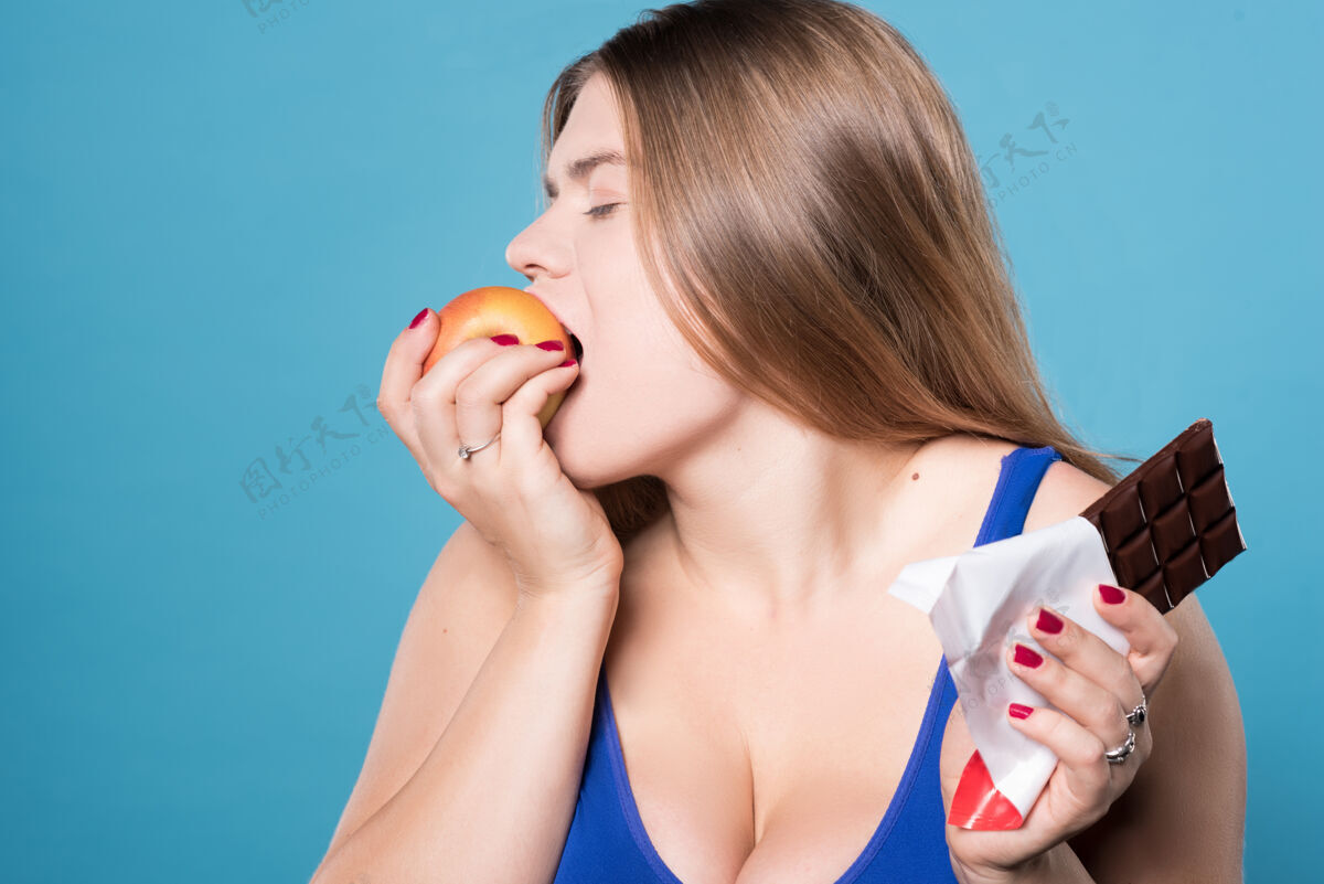 体重我做了我的选择关闭俯视特写镜头：年轻丰满的美女贪婪地吃着苹果 另一只手拿着巧克力美丽健身健康