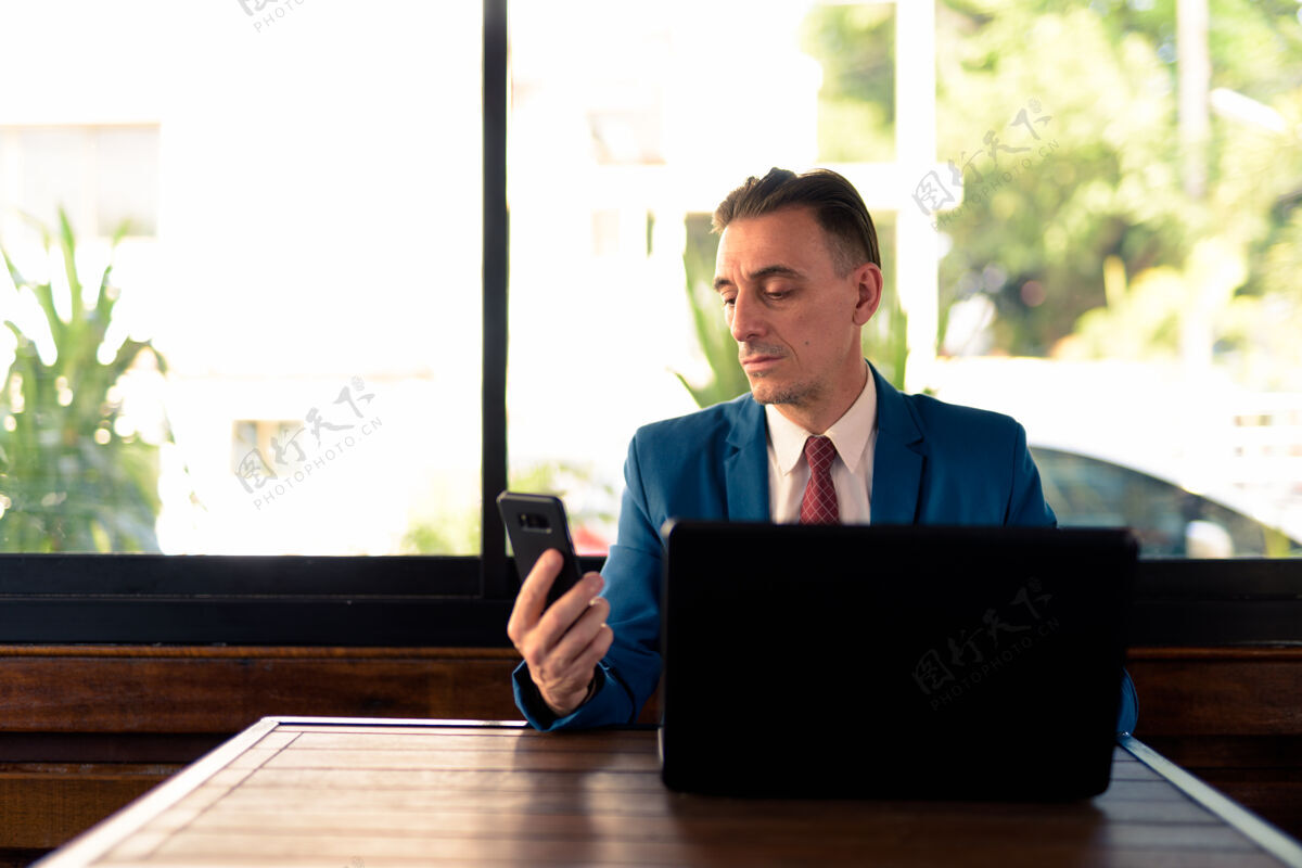 电脑成熟英俊的意大利商人在咖啡店放松的画像手持连接成熟