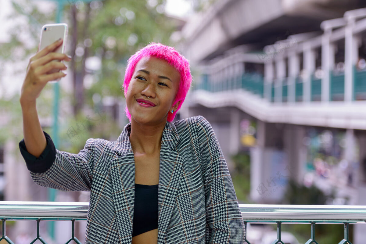 互联网年轻叛逆的亚洲女商人的肖像 粉红色的头发在城市户外的人行天桥上自拍行政20多岁