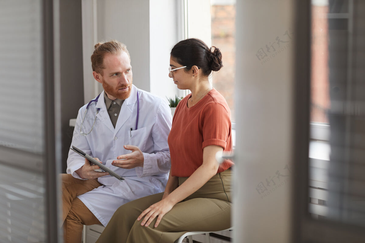 患者一位身穿白大褂的男医生坐在医院走廊上和他的病人说话医院医学医疗职业