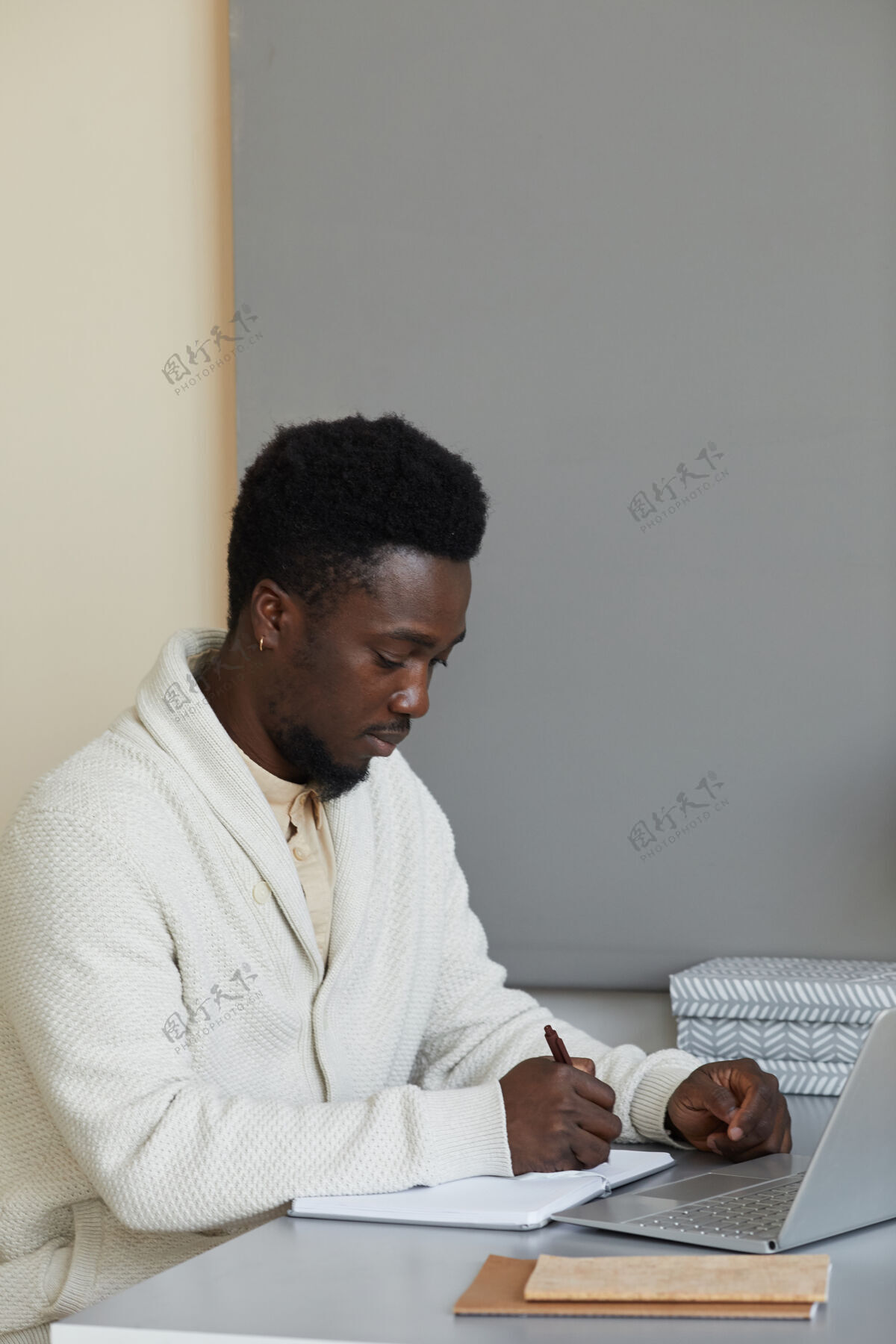 坐着坐在办公室里拿着笔记本电脑 在笔记本上写商业计划的非洲男人现代室内成人