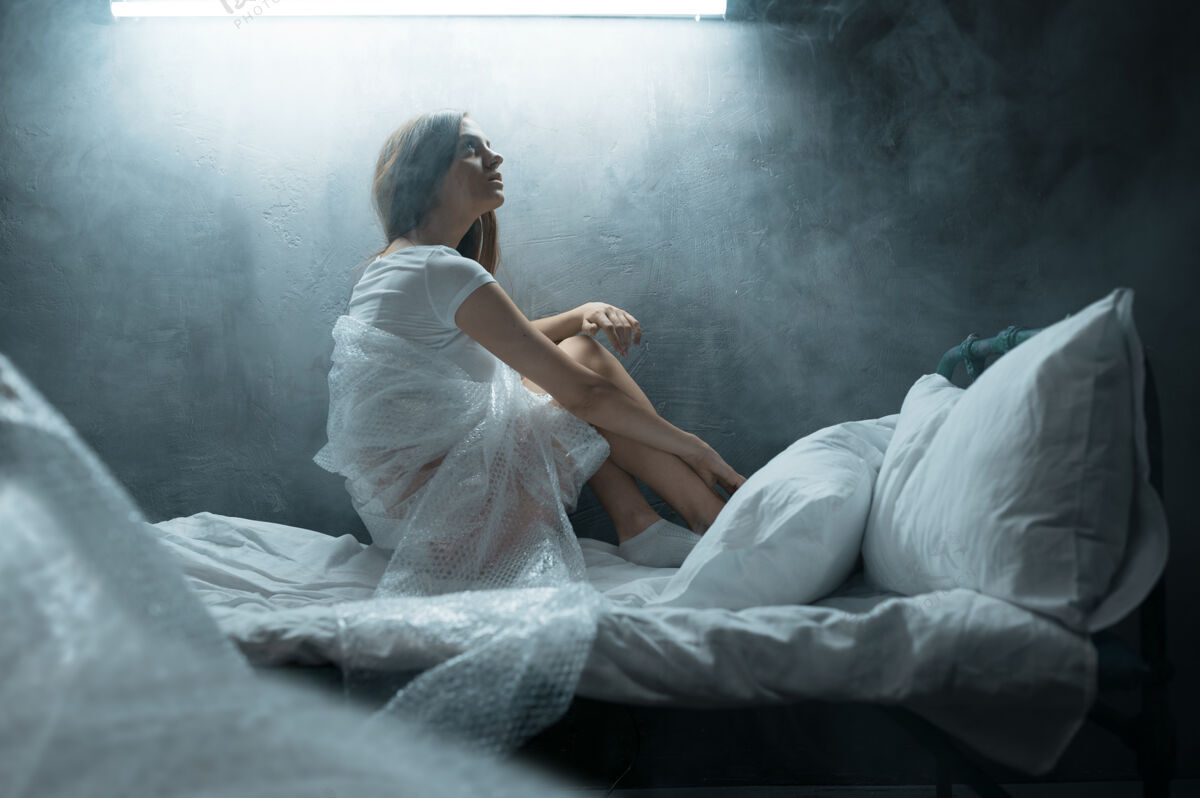 头痛精神病女人在包装膜里坐在床上 失眠 暗室…迷幻的女人每晚都有问题 抑郁和压力 悲伤 精神病医院人问题光