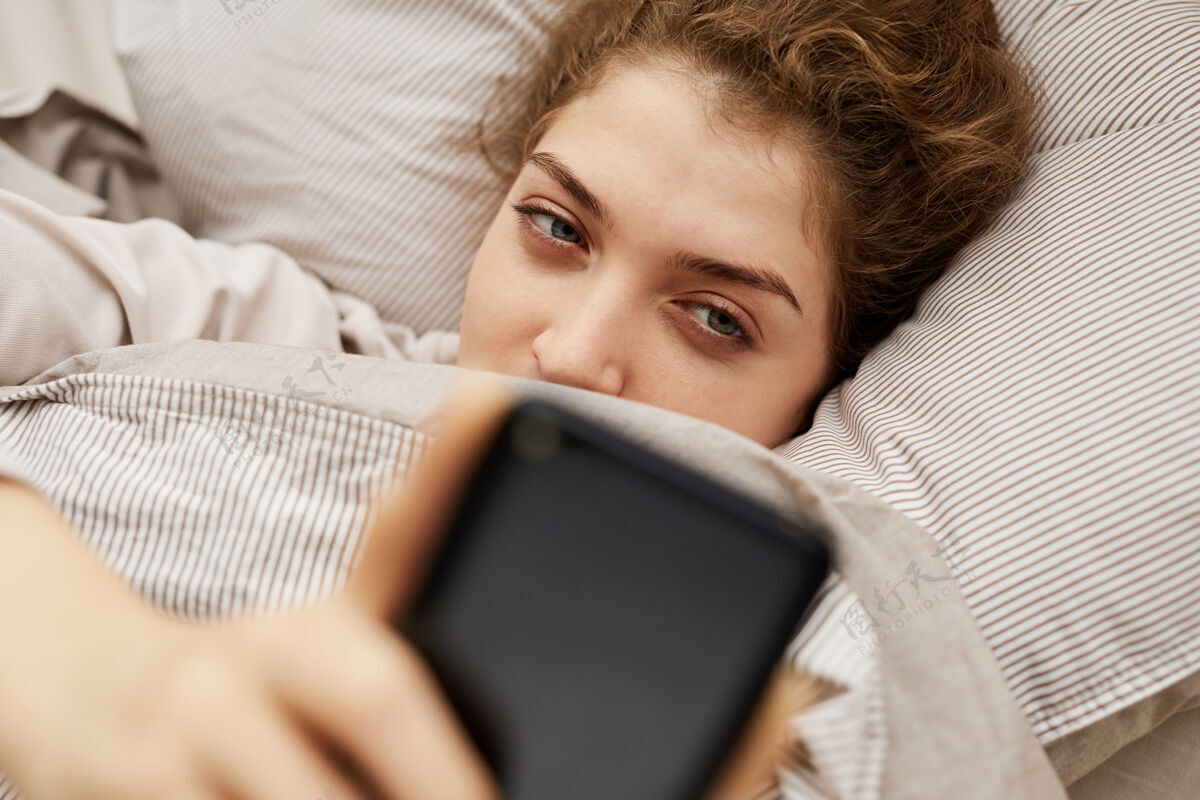 休闲服躺在床上用手机上网聊天的年轻女子抱人看