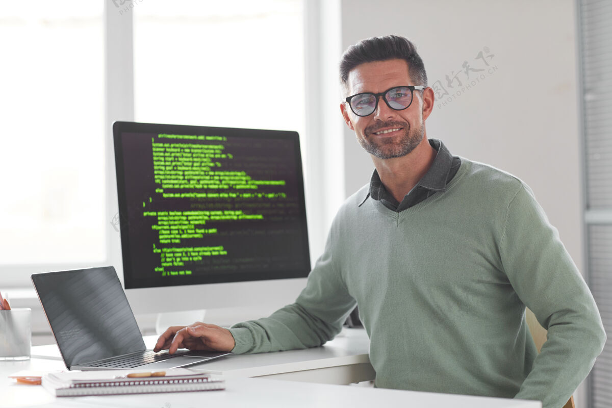 开发在开发新的计算机系统时 戴着眼镜的成熟的计算机程序员看着前面的画像欢呼系统微笑