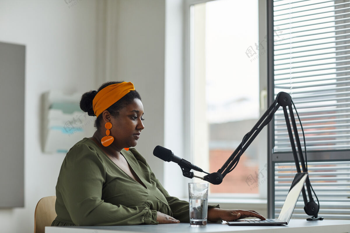 收音机年轻的电台主持人坐在笔记本电脑前的桌子旁 对着麦克风讲话 在电台工作商务职业使用电话