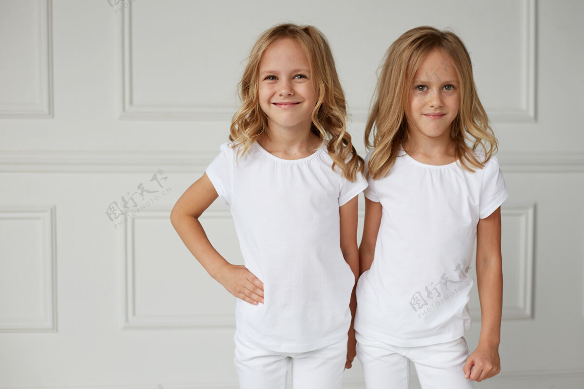 姐姐前面是两个穿着白衣服微笑的小女孩金发小孩子