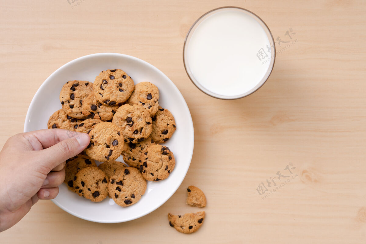 桌子一个从盘子里拿巧克力饼干 在木桌上拿牛奶的人烘焙饮料餐