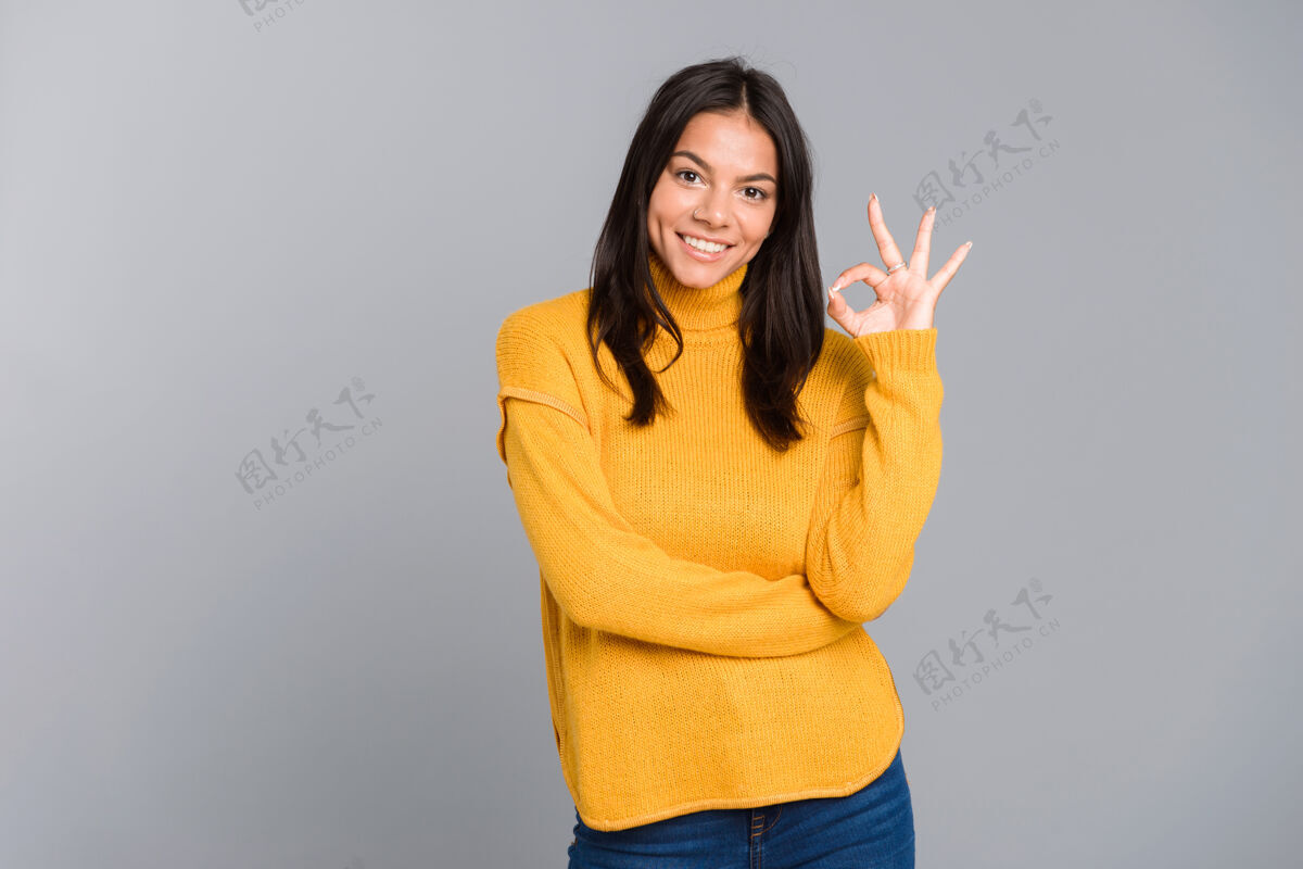 手一位身着毛衣 面带微笑的年轻女子孤零零地站在灰色墙壁上的画像 快乐展示休闲
