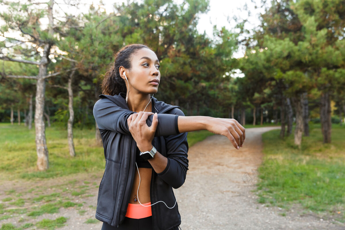 吸引力一幅20多岁的美籍非洲妇女穿着黑色运动服在绿色公园锻炼身体的照片美国保健耳机