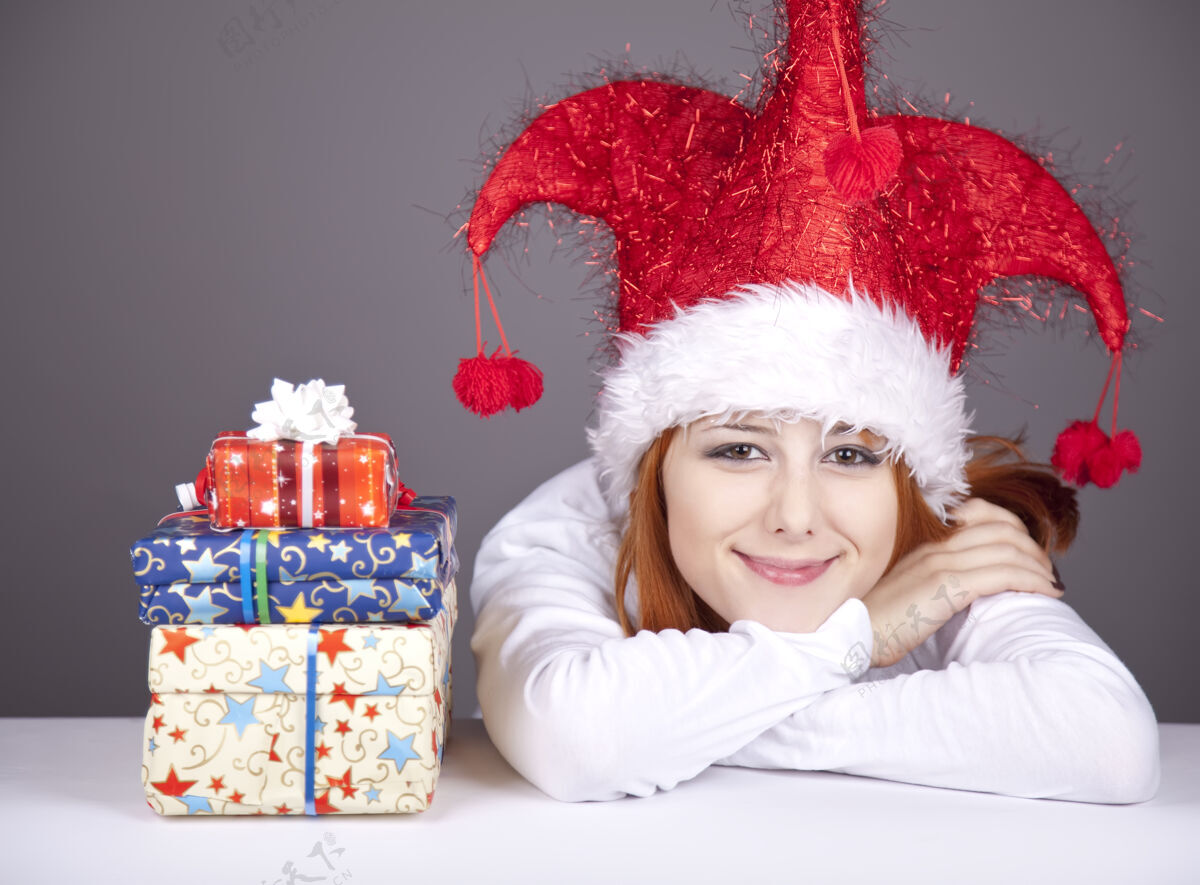 长滑稽的红发女孩戴着圣诞帽 手里拿着礼品盒节日圣诞节无忧无虑