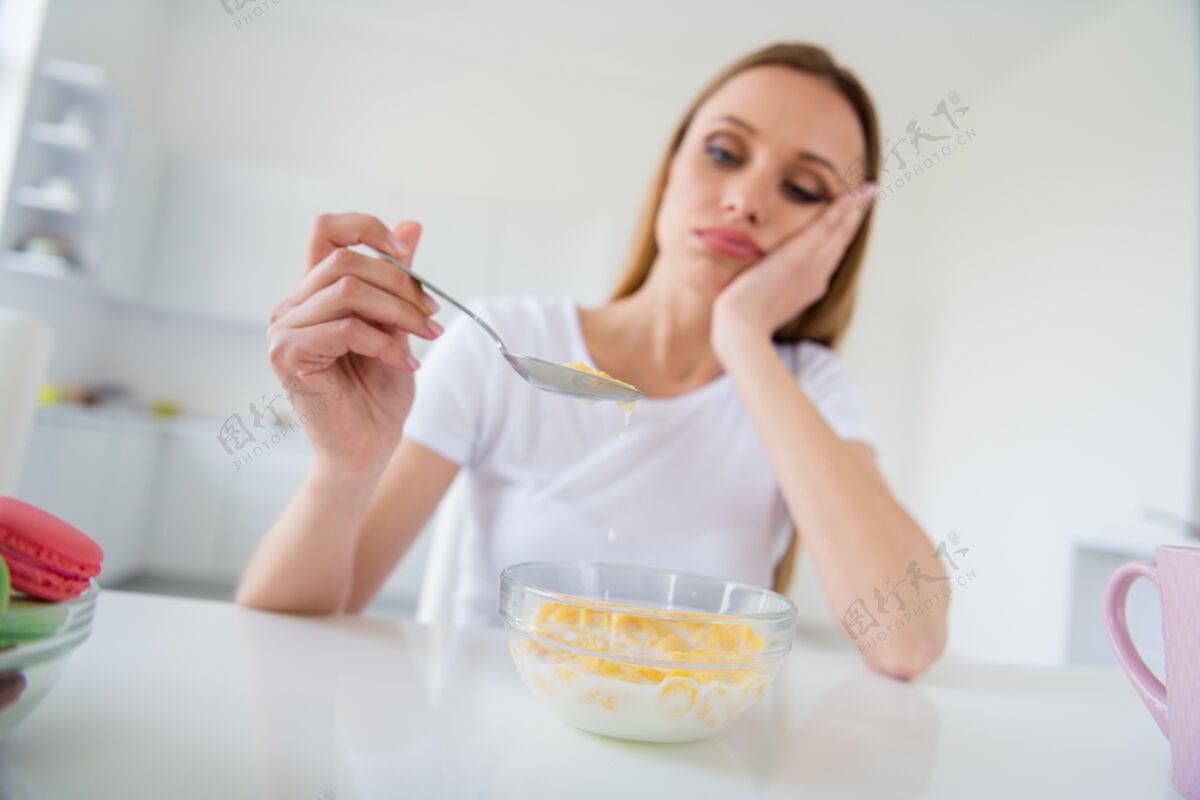 晚餐照片中美丽金发心烦意乱的主妇拿着勺子不想吃牛奶早餐玉米片厌倦节食无聊的餐桌白光厨房室内不开心格兰诺拉麦片零食