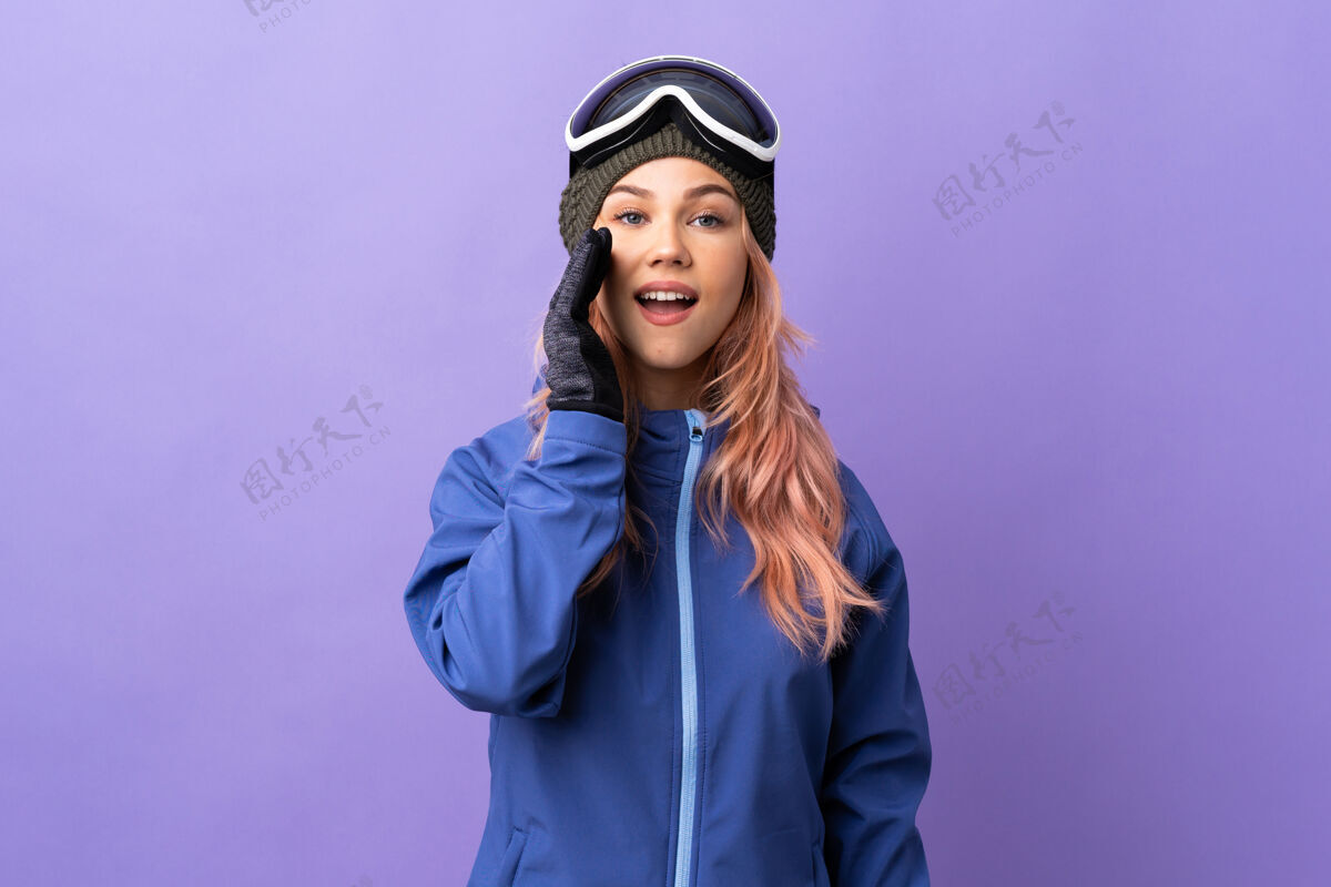 年轻滑雪者女孩戴着滑雪板上的眼镜孤立地张大嘴巴喊着紫色人信息运动