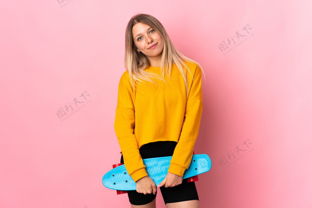 时尚年轻的金发女人穿着溜冰鞋被隔离在粉红色的地板上休闲酷娱乐
