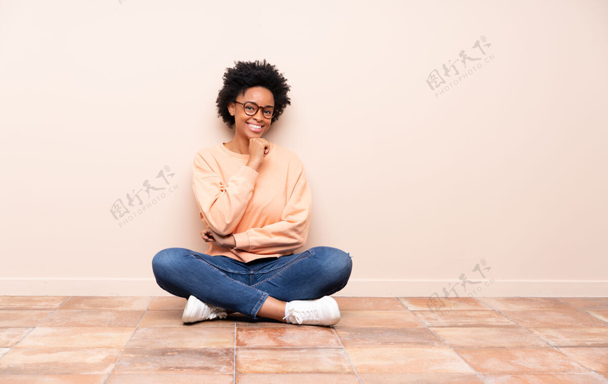 室内坐在地板上戴着眼镜微笑的非裔美国女人墙女人座位