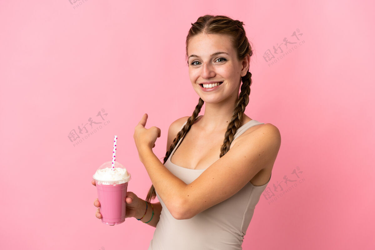 饮料一个年轻的女人用草莓奶昔隔离在粉红色的指尖后面看冰沙水果