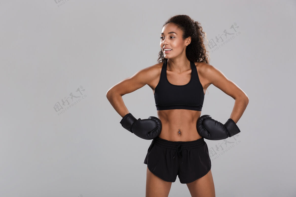 成人一个黑人年轻健美的女运动员在灰色背景下孤立地打拳击 目光转向别处女性强壮吸引力