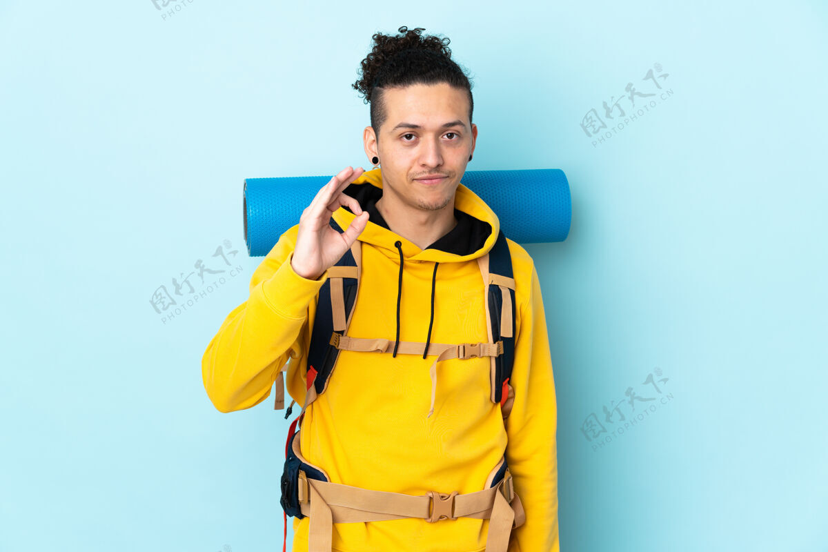 人一个年轻的登山者 背着一个大背包 在孤立的蓝色背景上 用手指画着“ok”的手势Ok旅游拉丁语