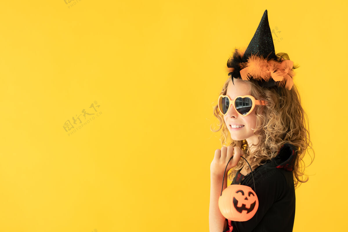 魔术师身着女巫服装的美丽女孩的画像映衬在黄色的表面上庆祝服装复制空间