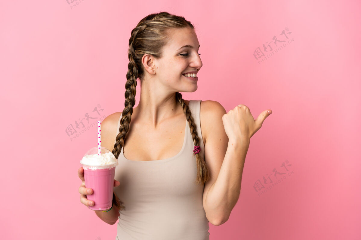 手势年轻女子用草莓奶昔孤立地指着粉色的一面来呈现产品杯子人女性