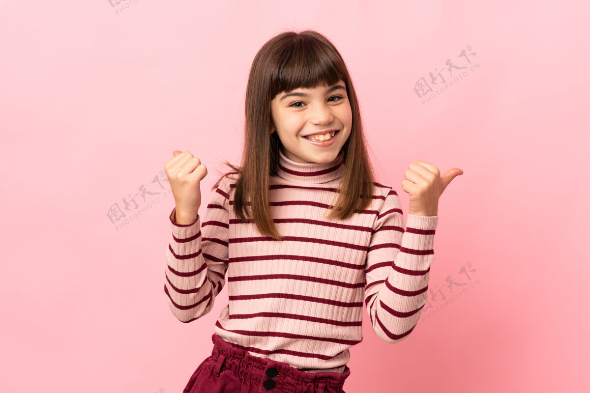 积极小女孩孤立的粉红色背景与拇指向上的手势和微笑拇指墙壁女孩