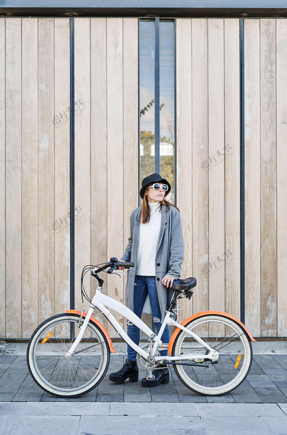 复古一个年轻漂亮的白人女孩 穿着灰色夹克 白色毛衣 戴着帽子在城里骑自行车女人户外太阳镜