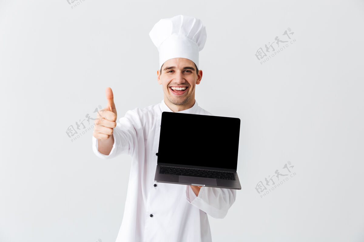 白种人开朗的厨师身穿厨师制服站在白色的墙上 手里拿着银行屏幕的笔记本电脑显示网络服务