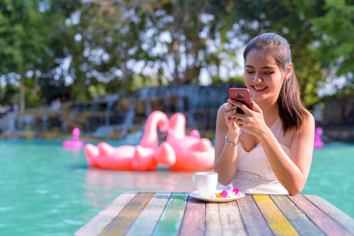 泰国年轻美丽的亚洲女游客在湖边户外放松的画像快乐成人火烈鸟