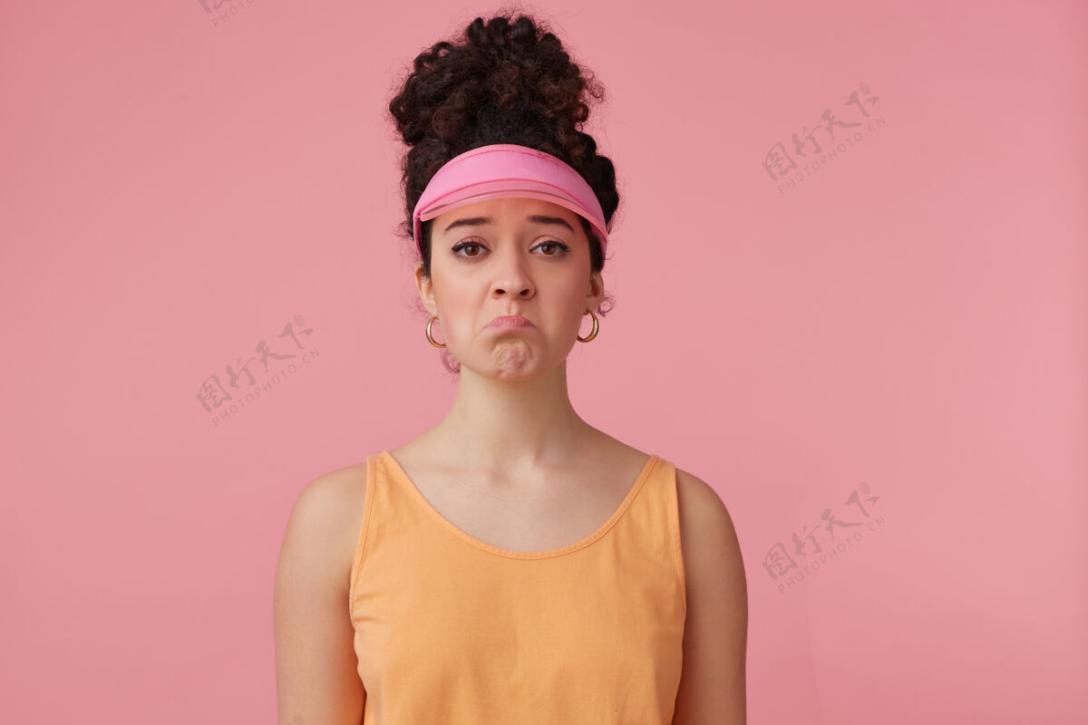 完美悲伤女孩的肖像 黑色卷发 发髻 戴粉色帽舌 耳环和橙色背心 化妆 情感概念 撅着嘴唇T恤女人20多岁