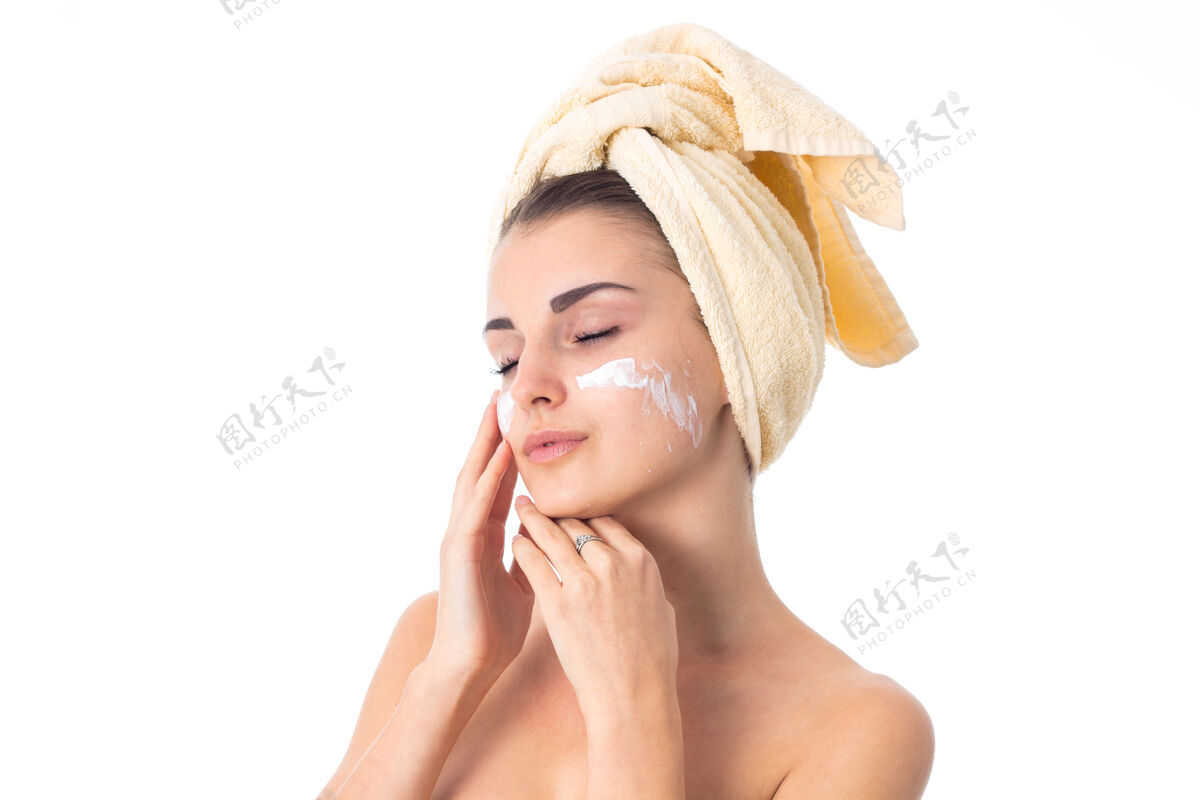 触摸可爱的女人用毛巾在头上涂上隔离在白墙上的乳霜来护理她的皮肤健康毛巾微笑