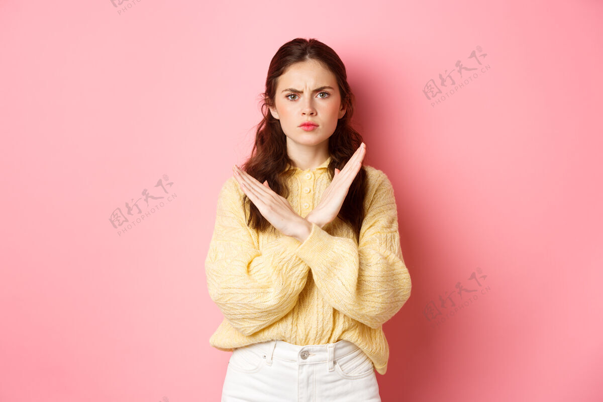 成人严肃的年轻女子皱着眉头 神情坚定 做出交叉阻挡的手势 禁止做坏事 说不 站在粉红色的墙上否认乐观姿态